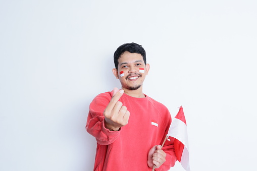 Indonesian man showing excitement with mini heart sign when celebrating independence day, isolated on white background.