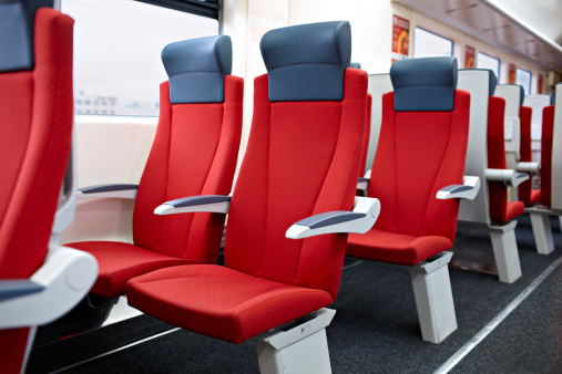 An interior view of  a modern high speed train. Red chairs.