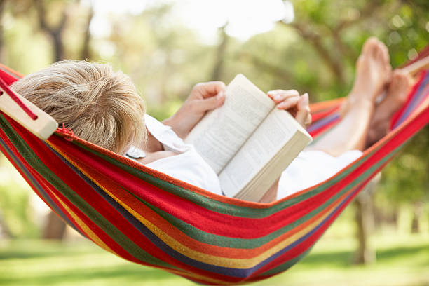Teenage girl resting in back yard on a summer day. She is reading a book.\nCanon R5