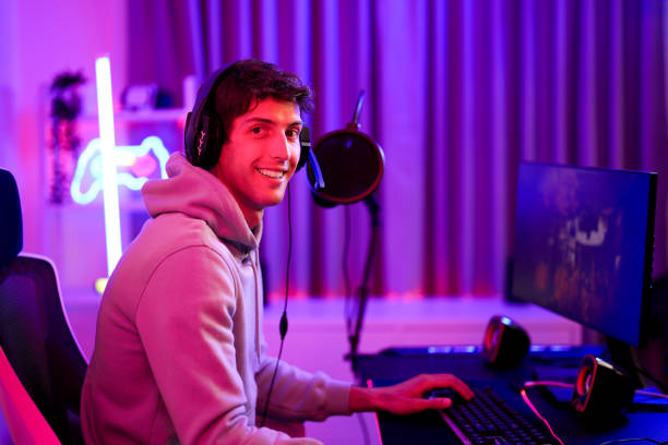 istock Professional gamer handsome smile while playing video game with online friend and use wireless headset listening music and sound in neon pink room 1591210280