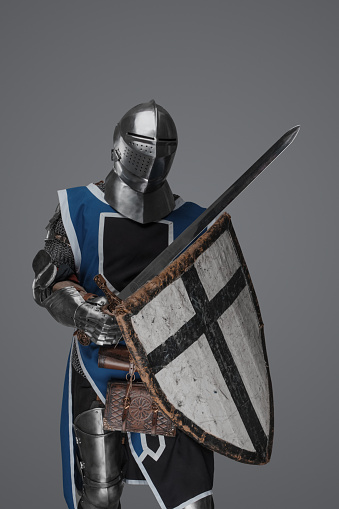 Blue surcoat-wearing medieval knight actively swinging sword in battle on gray background