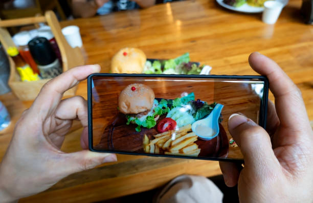 istock Young blogger  man hand using smartphone take picture in the restaurant 1591258795