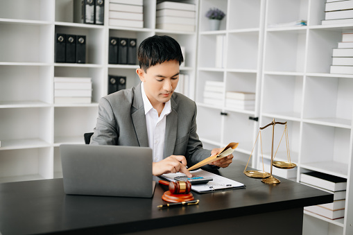 justice and law concept. Asian businessman or lawyer or accountant working on accounts using a smart phone laptop digital tablet calculator and documents in modern office
