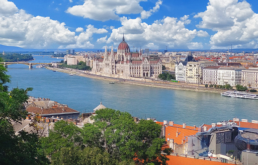 The image shows a beautiful view of the Hungarian Parliament Building, which is located on the banks of the Danube River in Budapest. The building is a stunning example of Gothic Revival and Renaissance Revival architecture, and it is one of the most popular tourist destinations in Hungary.\nWe see the Parliament Building from a distance, and it captures the building's imposing size and grandeur. The building is made of white stone, and it has a large dome that dominates the skyline. \nWe also see the Danube River, which flows past the Parliament Building. The river is a deep blue color, and it is dotted with boats and other watercraft. The riverbank is lined with trees and buildings, and it provides a beautiful setting for the Parliament Building.\nThe image is a stunning depiction of one of Hungary's most iconic landmarks. It captures the beauty of the Parliament Building and the Danube River, and it is a reminder of the rich history and culture of Budapest.