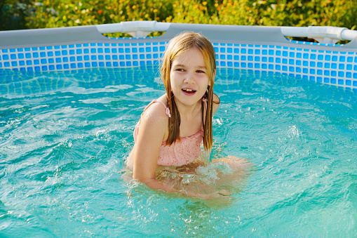 Cute teenage girl in pink swimsuit playing in a small pool. Swimming pool for the garden or yard in a country house.