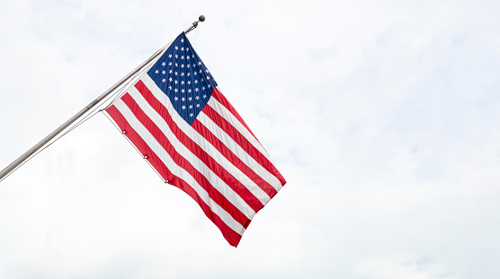 United States of America flag on a pole waving on cloudy sky background. USA sign symbol