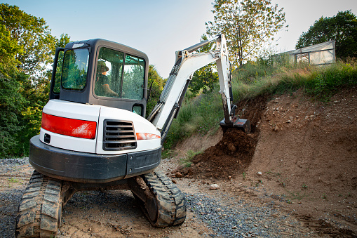 Worker digging up dirt with compact excavator