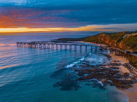 Sunrise seascape with cloud filled sky and the old coal loading jetty at Catherine Hill Bay on the Central Coast of NSW, Australia.