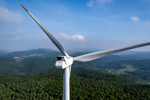 A close-up bird's-eye view of a wind turbine on a forest covered mountain on a clear day