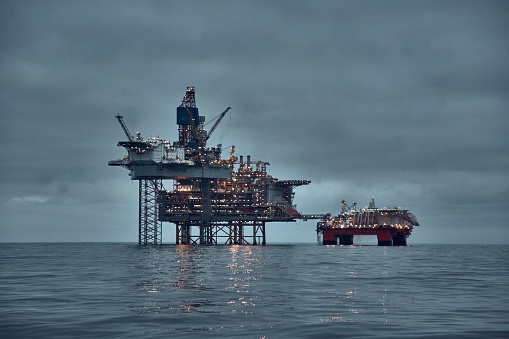 North Sea oil and gas production. Oil and gas platform, jack up rig in the sea at dusk with dark sky and clear water surface.