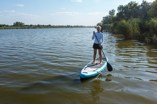 Woman paddling on SUP board on beautiful lake.