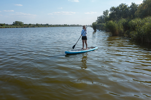 Woman paddling on SUP board on beautiful lake.