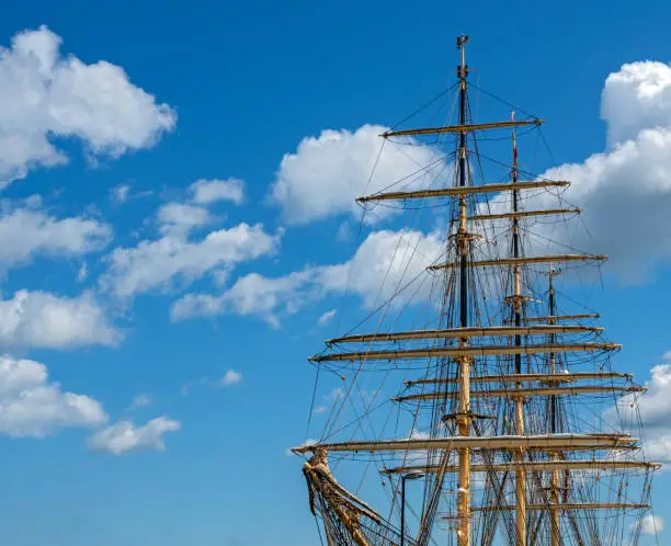 masts and rigging of a three-masted sailing ship before a blue sky with white clouds