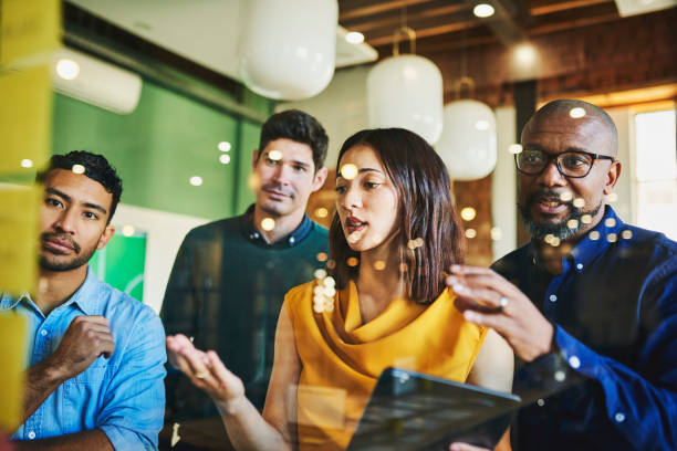istock Bearded manager and colleagues reading sticky notes on glass wall in office 1591572457