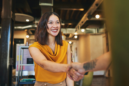 Businesswoman smiling cheerfully and shaking hands with client in meeting room