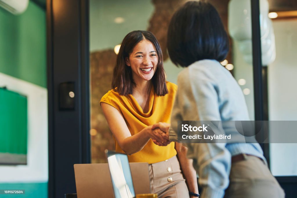 Cheerful businesswomen shaking hands in meeting room Businesswoman shaking hands with client and smiling cheerfully in meeting room Business Stock Photo