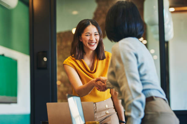 Cheerful businesswomen shaking hands in meeting room Businesswoman shaking hands with client and smiling cheerfully in meeting room greeting stock pictures, royalty-free photos & images