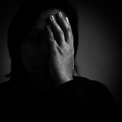 Dark female portrait with hand covering half of face.