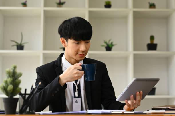 istock Male economist drinking coffee and using digital tablet, working with sales statistics document at office desk. 1591588383