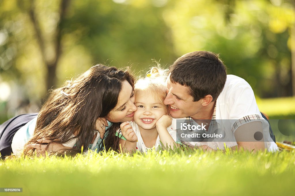 Happy mother and father kissing their daughter in the park Adult Stock Photo