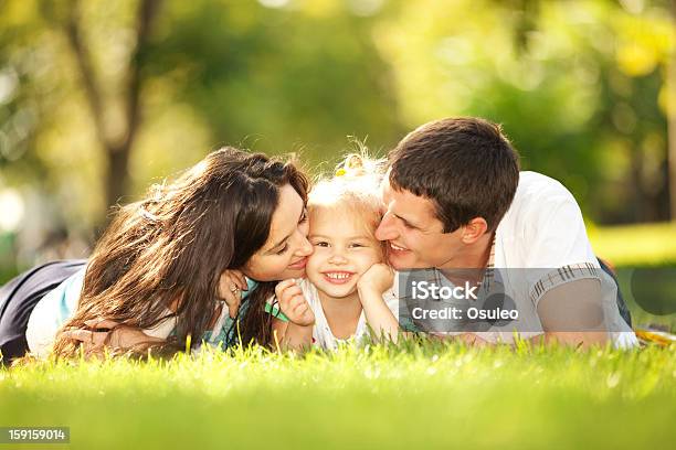 Happy Mother And Father Kissing Their Daughter In The Park Stock Photo - Download Image Now