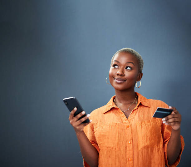 istock Thinking, ecommerce and credit card with a black woman using her phone in studio on a gray background. Mobile, online shopping and finance payment with a female shopper searching for a deal or sale 1591599053