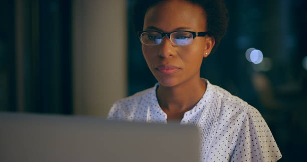 istock Business woman, computer and working at night with glasses for programming, research or deadline. Dark office, technology and face of serious software engineer person reading information for coding 1591625072