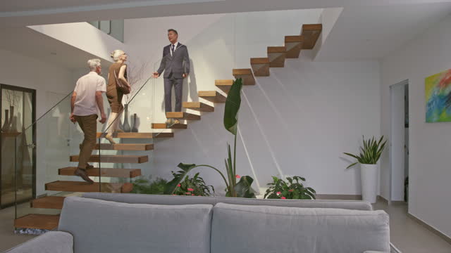 DS Male real estate agent walking up the staircase with his clients in the luxury house