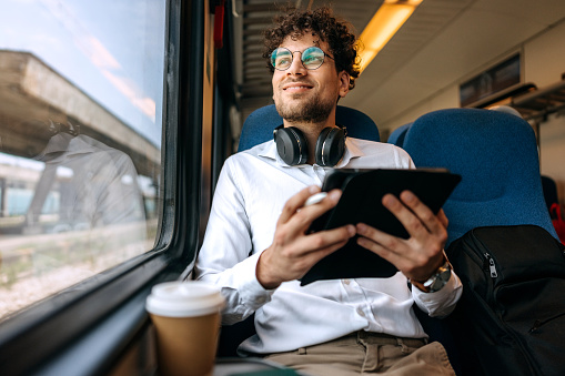 Casually clothed handsome man using digital tablet while riding in a train