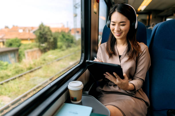 istock Smiling beautiful woman with headphones using digital tablet while riding in a train 1591657991