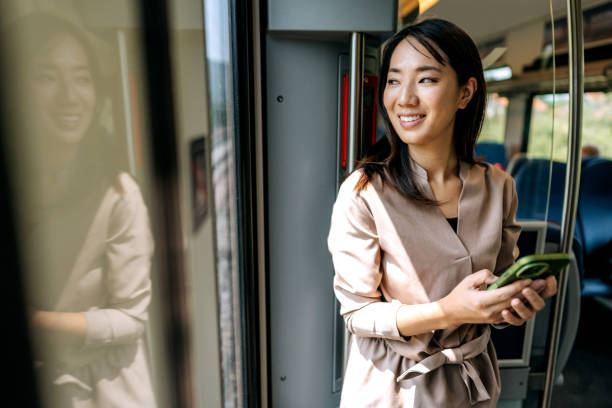 istock Smiling beautiful Japanese woman using phone while riding in a train 1591658092