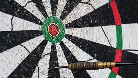 close up of a dart arrow next to bulls-eye on a dartboard as precision, training, leisure, marketing concept with copy space