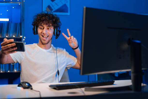 istock Arabic guy gamer in a headset playing computer games sits at a computer at night and makes a video call on a smartphone, shows a greeting gesture 1591662361