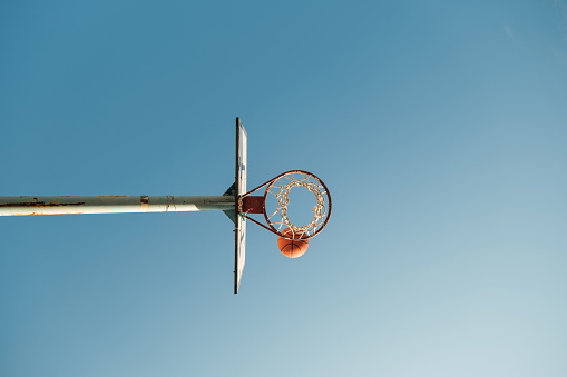 From below of basketball hoop with net on ring and orange ball against cloudless clear sky