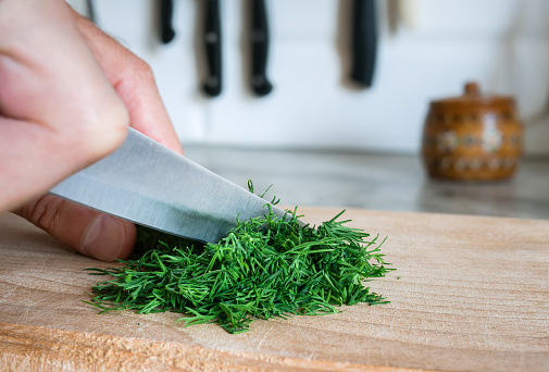 Chopping dill with a knife on a beech cutting board