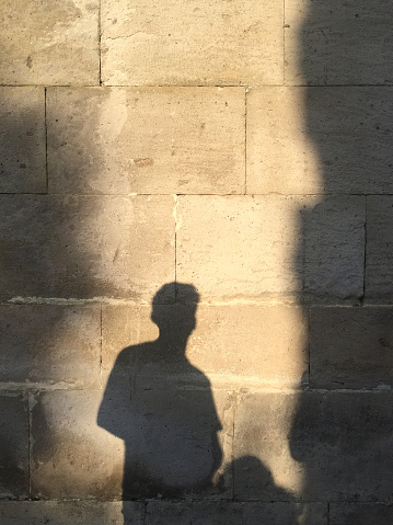 People shadow on the old stone wall with sunlight reflection at sunset