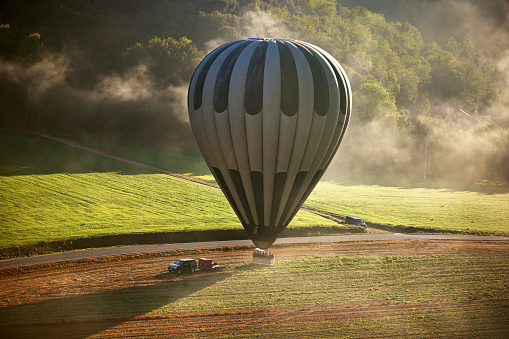 Elevated perspective from companion balloon floating over agricultural field illuminated by sunlight and low-lying fog, Province of Girona, Spain.