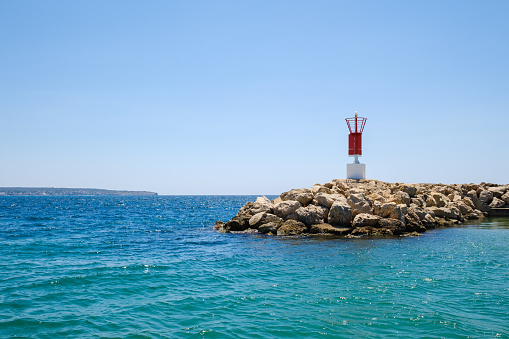 Scenic view of red beacon located on rocky shore washed by turquoise rippling sea water under cloudless blue sky