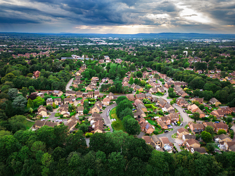 Aerial image taken by drone depicting detached houses in a residential area - specifically in Crawley, close to Gatwick Airport in West Sussex. The houses are surrounded by lush green trees.