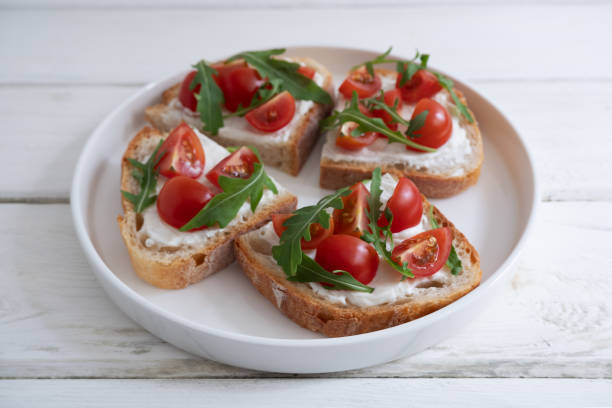 istock Cherry tomato toast with cream cheese and arugula on wheat bread in a white plate on a light background. Healthy breakfast, Proper nutrition. 1591712144