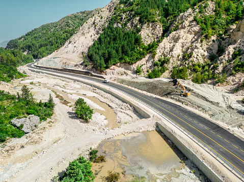 Mountain pass road under construction with excavators and heavy trucks working on construction site, aerial view in Albania.