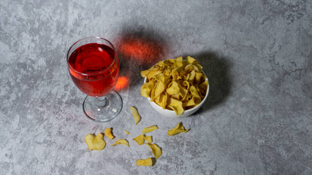 sirop rouge aromatisé à la framboise dans une tasse en verre et chips de manioc dans un bol en plastique blanc isolé sur fond gris - editorial label man made material healthcare and medicine photos et images de collection