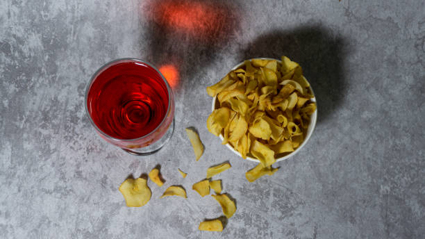 sirop rouge aromatisé à la framboise dans une tasse en verre et chips de manioc dans un bol en plastique blanc isolé sur fond gris - editorial label man made material healthcare and medicine photos et images de collection