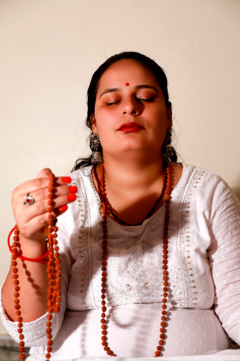 Female monk holding rudraksha beads in hands during meditation eyes closed portrait.