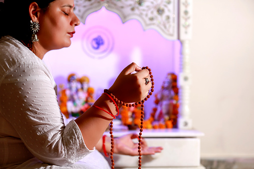 Mid adult female monk of Indian ethnicity worshiping in temple holding rudrakasha beads.