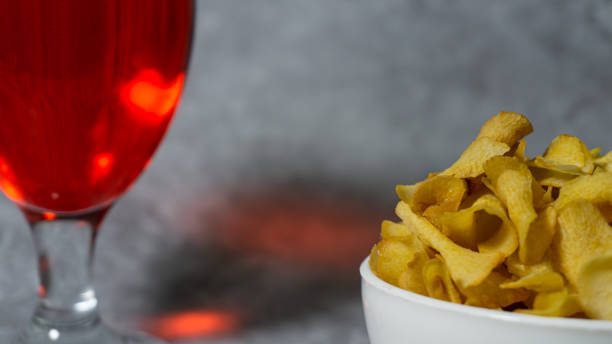 sirop rouge aromatisé à la framboise dans une tasse en verre et chips de manioc dans un bol en plastique blanc isolé sur fond gris - editorial label man made material healthcare and medicine photos et images de collection