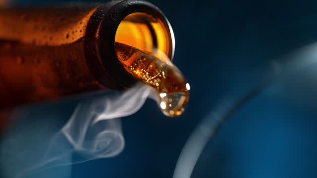 Pouring Beer to Glass - Bottle Tilts and Fog of Gas Comes Out in Slow Motion on Dark Blue Background