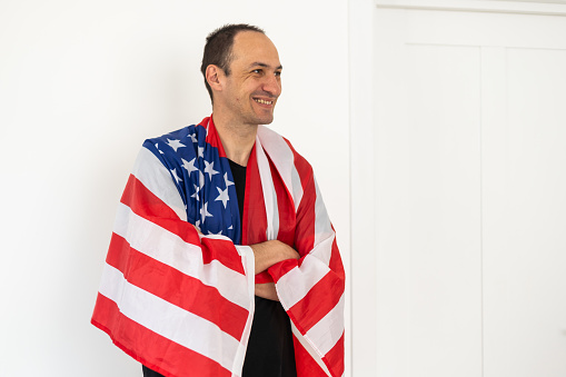 White guy holding a flag of United States smiling confident with crossed arms isolated on a white background. High quality photo