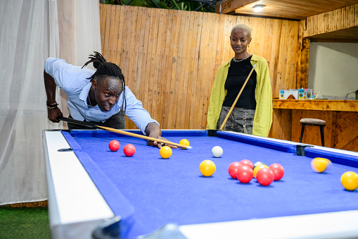 Young African man preparing to shoot and female competitor watching as they play English eight-ball.