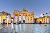 Brandenburg Gate in Berlin, Germany at night with wet ground and blue sky.